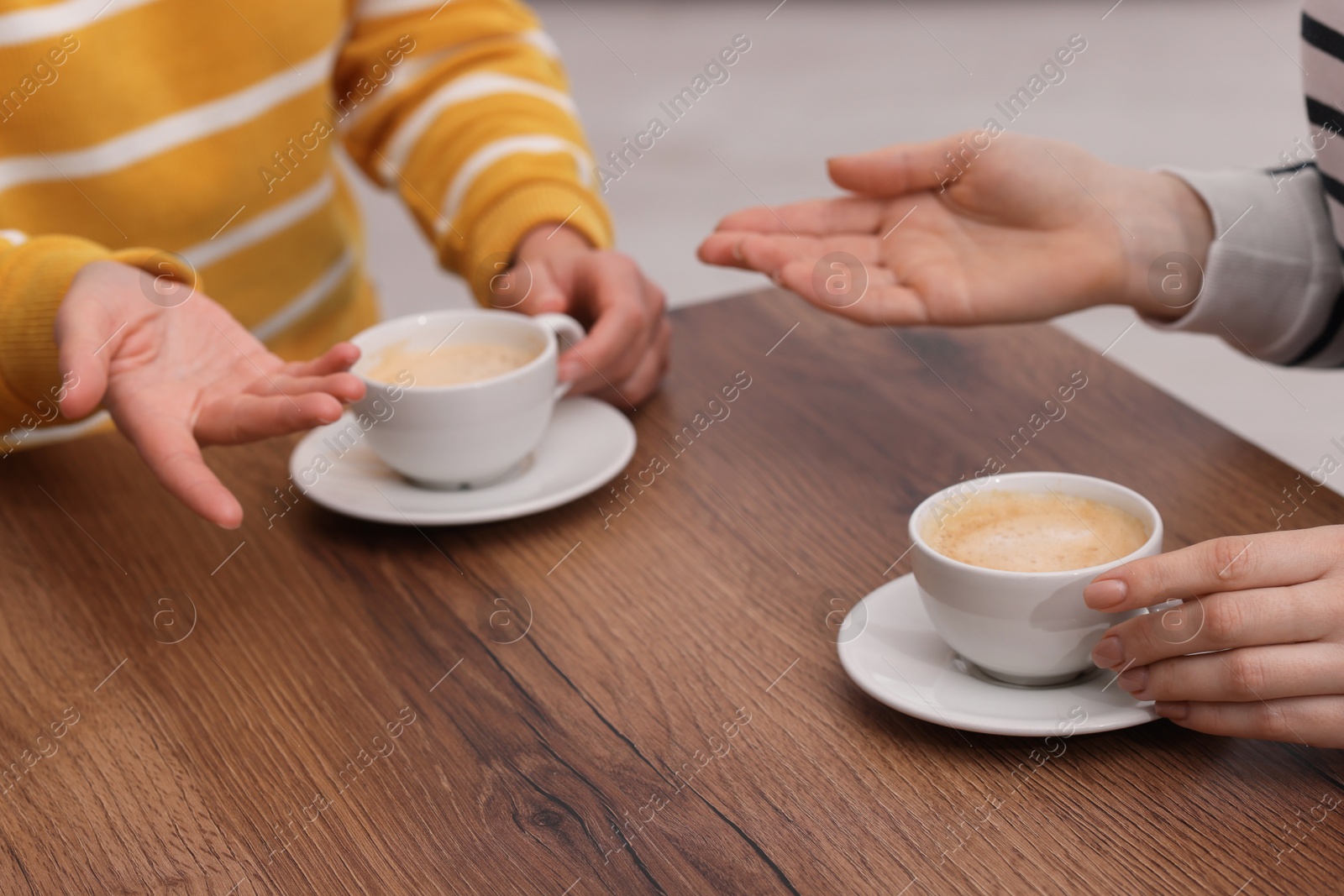 Photo of Coffee break. Women with cups of hot drinks at wooden table indoors, closeup