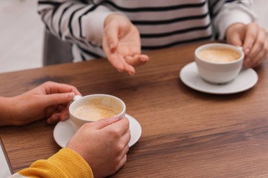 Photo of Coffee break. Women with cups of hot drinks at wooden table indoors, closeup