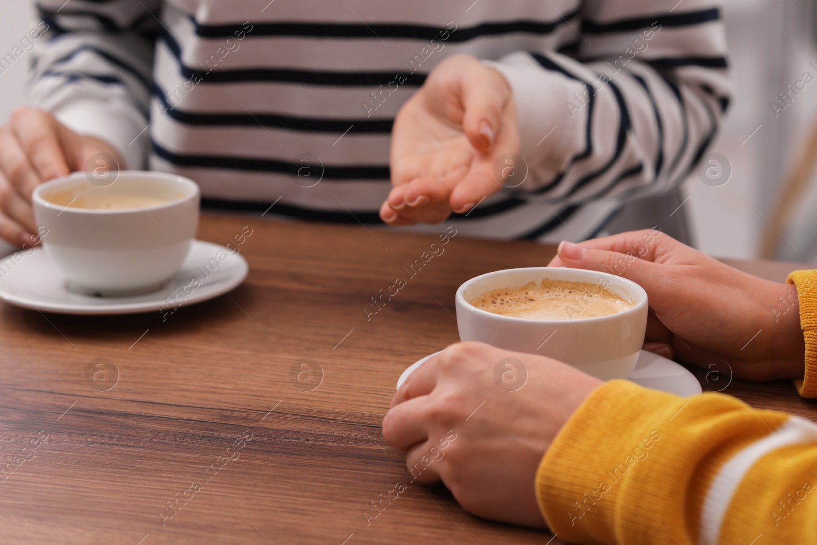 Photo of Coffee break. Women with cups of hot drinks at wooden table indoors, closeup