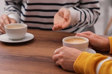 Photo of Coffee break. Women with cups of hot drinks at wooden table indoors, closeup