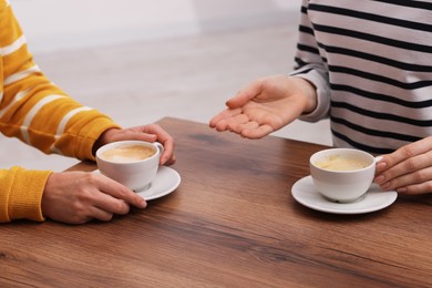 Photo of Coffee break. Women with cups of hot drinks at wooden table indoors, closeup