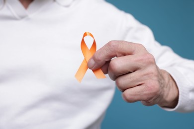 Photo of Multiple Sclerosis awareness. Senior man with orange ribbon on light blue background, closeup