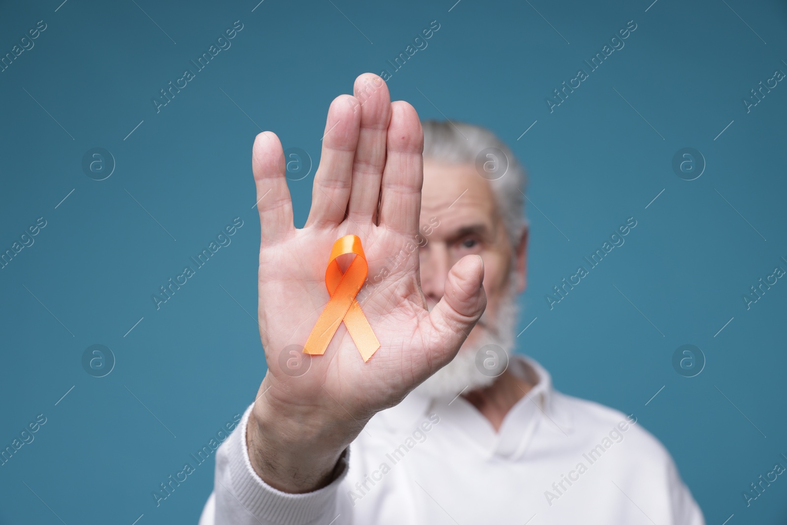 Photo of Multiple Sclerosis awareness. Senior man with orange ribbon on light blue background, selective focus