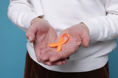 Photo of Multiple Sclerosis awareness. Senior man with orange ribbon on light blue background, closeup