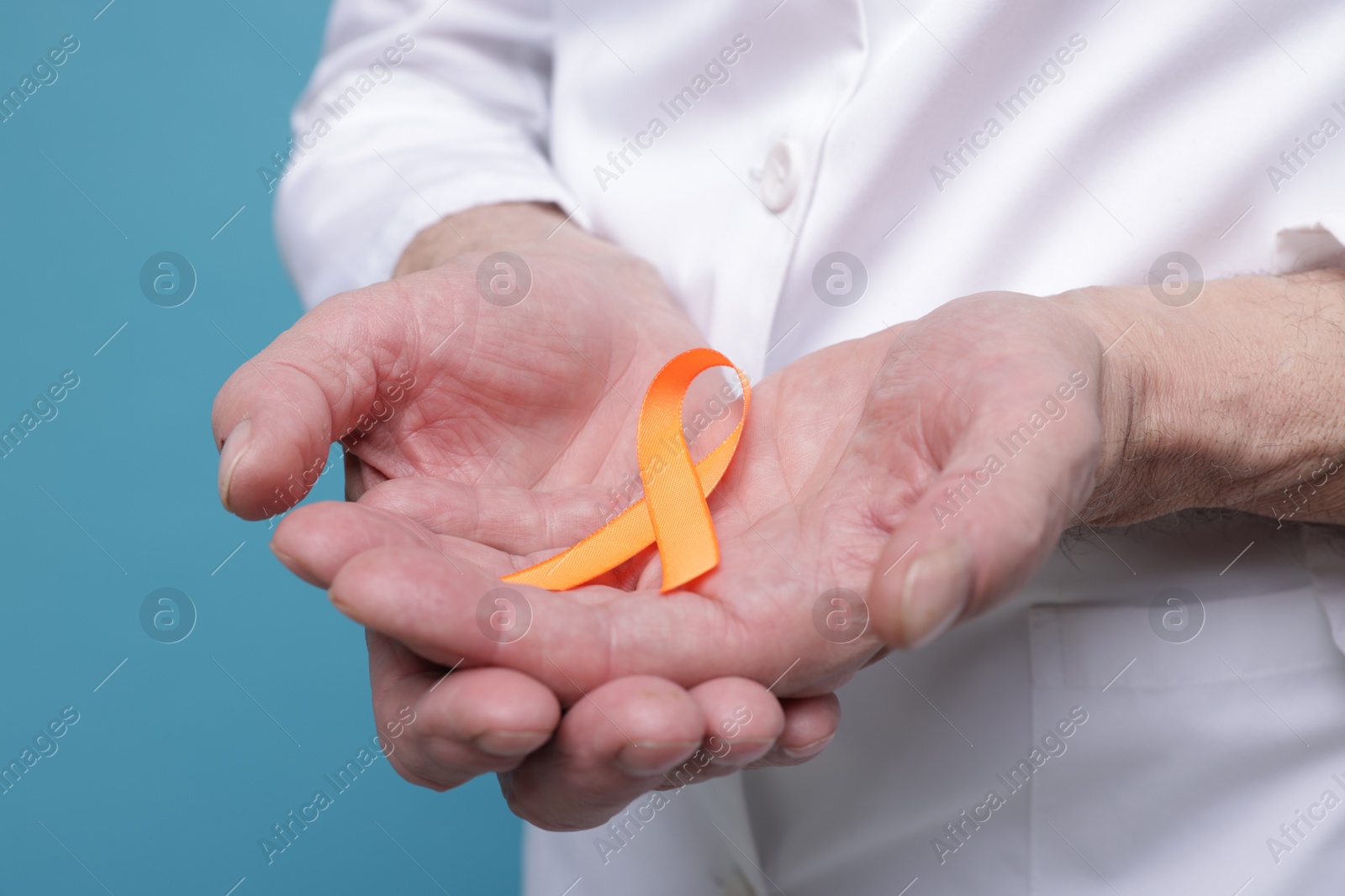 Photo of Multiple Sclerosis awareness. Doctor with orange ribbon on light blue background, closeup