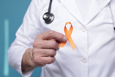 Photo of Multiple Sclerosis awareness. Doctor with orange ribbon on light blue background, closeup