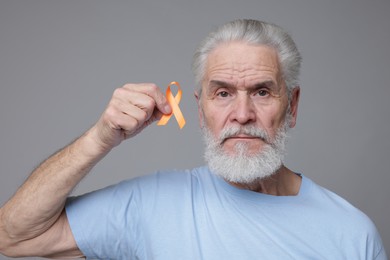 Photo of Multiple Sclerosis awareness. Senior man with orange ribbon on grey background