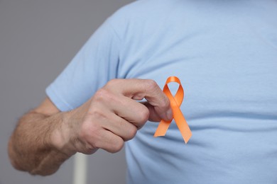 Photo of Multiple Sclerosis awareness. Senior man with orange ribbon on grey background, closeup