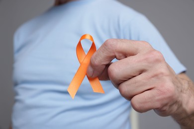 Photo of Multiple Sclerosis awareness. Senior man with orange ribbon on grey background, closeup