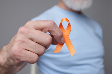 Photo of Multiple Sclerosis awareness. Senior man with orange ribbon on grey background, closeup