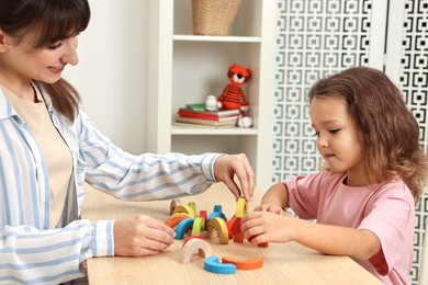 Photo of Autism therapy. Smiling psychologist and little girl playing with educational toy at table in mental health center