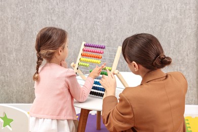 Photo of Autism therapy. Psychologist and little girl playing with wooden abacus indoors, back view