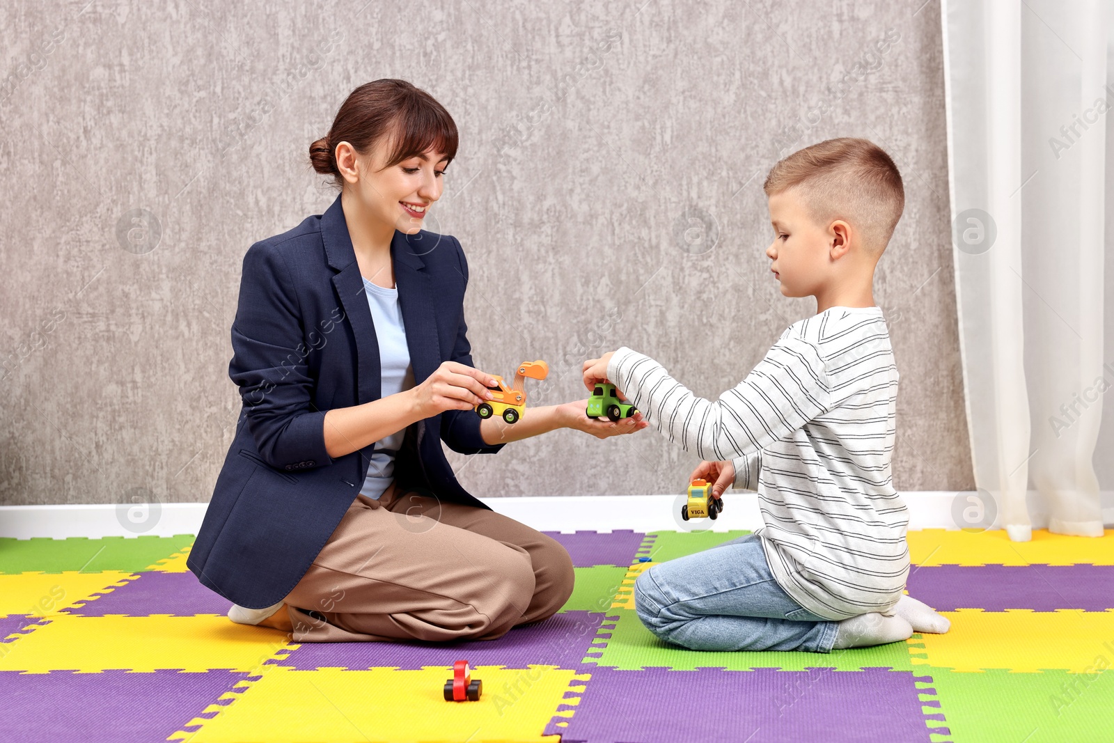 Photo of Autism therapy. Smiling psychologist and little boy playing with toy cars in mental health center