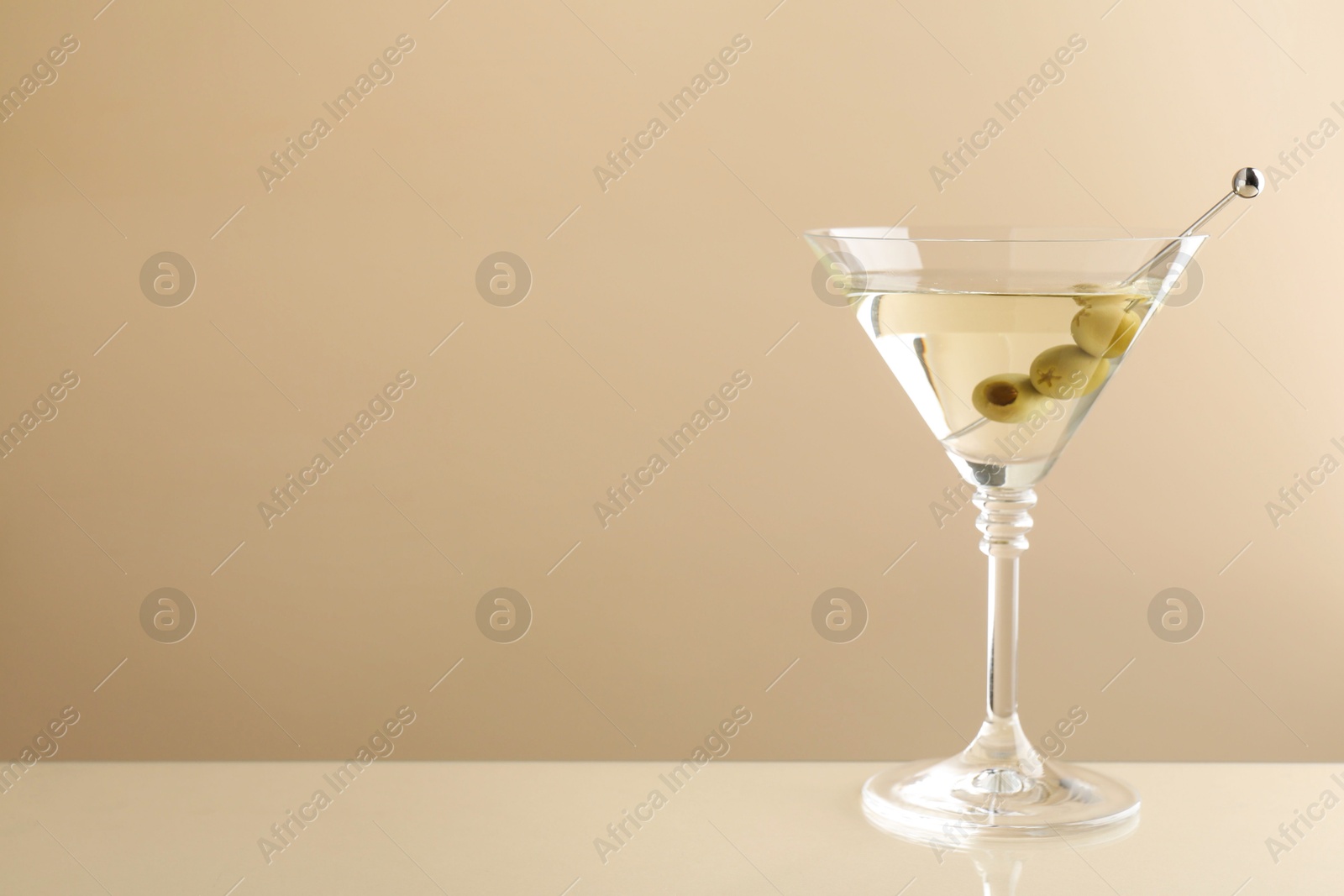 Photo of Martini cocktail with olives in glass on beige table, space for text