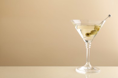 Photo of Martini cocktail with olives in glass on beige table, space for text