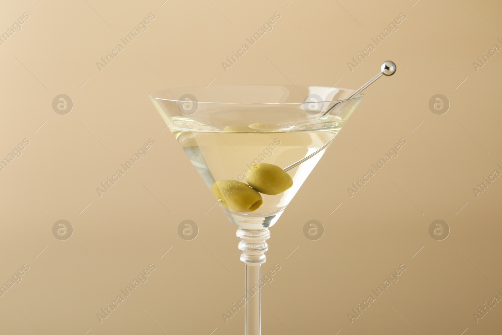 Photo of Martini cocktail with olives in glass on beige background, closeup