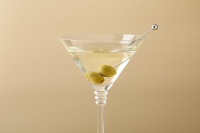 Photo of Martini cocktail with olives in glass on beige background, closeup