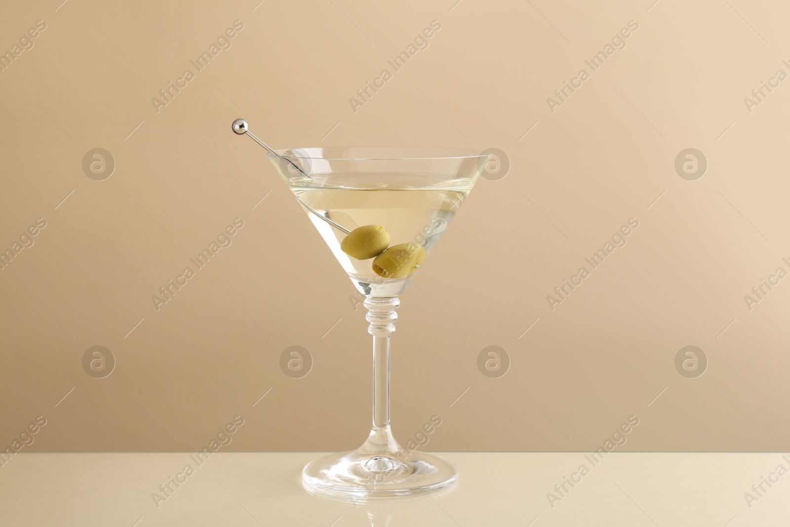 Photo of Martini cocktail with olives in glass on beige table