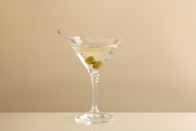 Photo of Martini cocktail with olives in glass on beige table