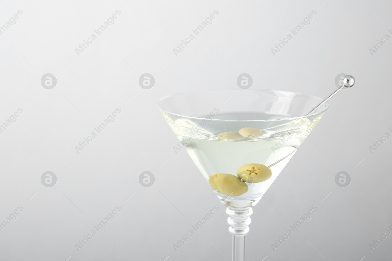 Photo of Martini cocktail with olives in glass on light grey background, closeup. Space for text