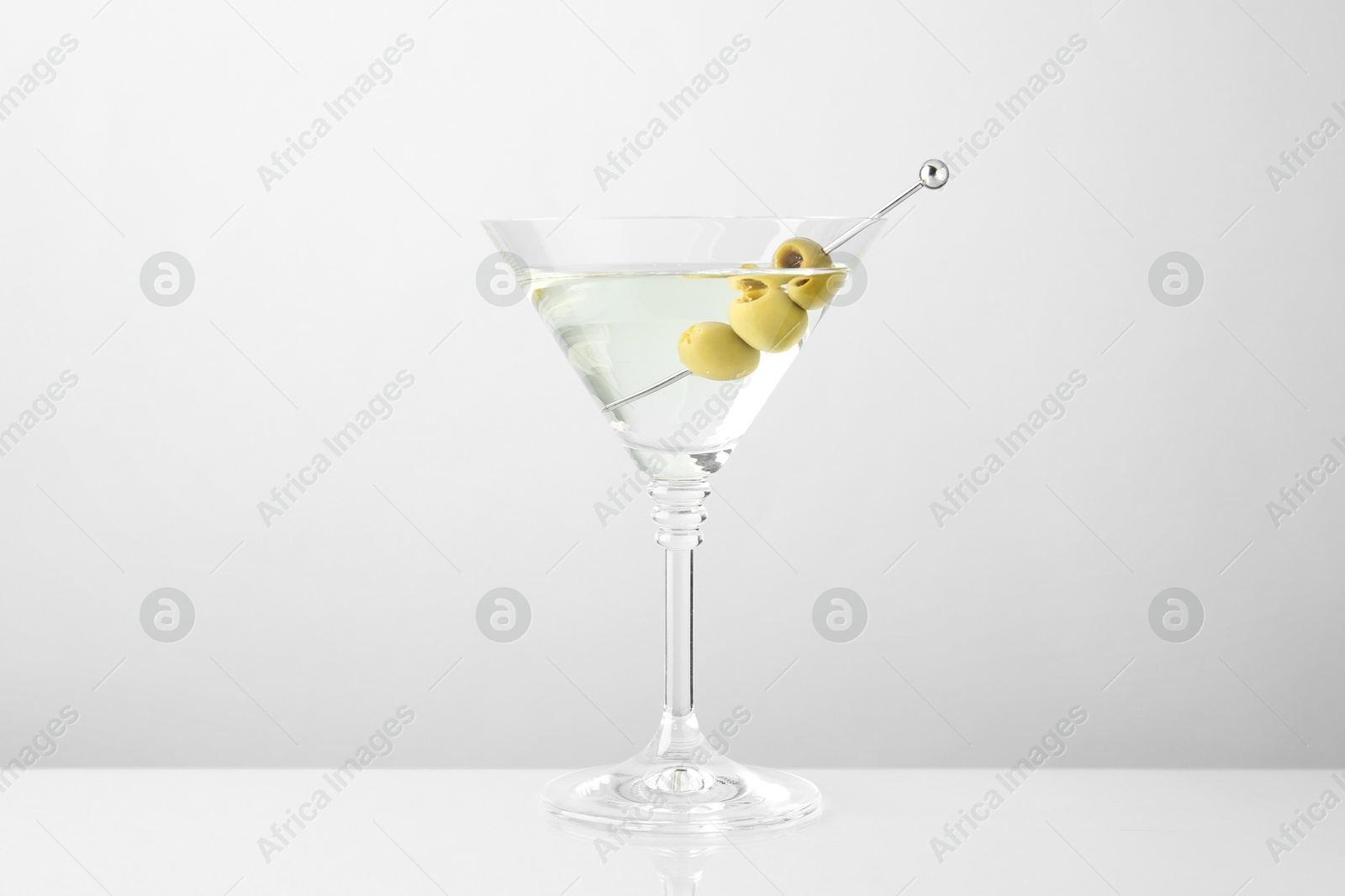 Photo of Martini cocktail with olives in glass on light table