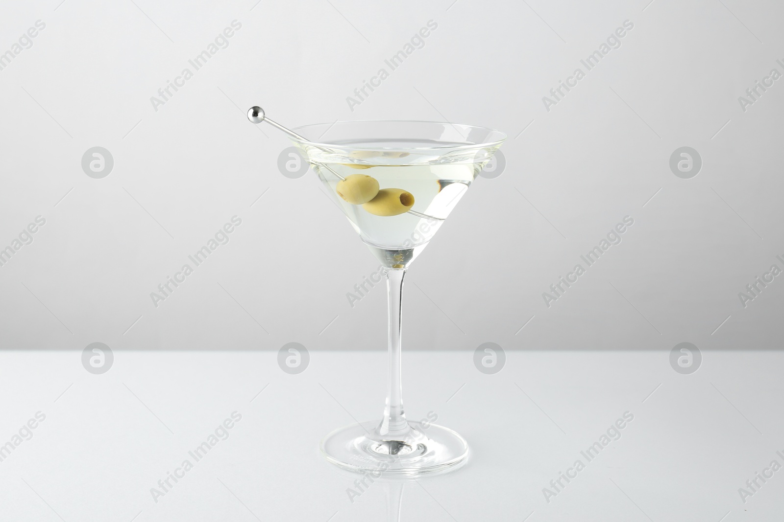 Photo of Martini cocktail with olives in glass on light table