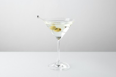 Photo of Martini cocktail with olives in glass on light table