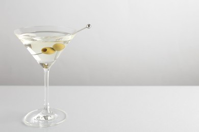 Photo of Martini cocktail with olives in glass on light table, space for text