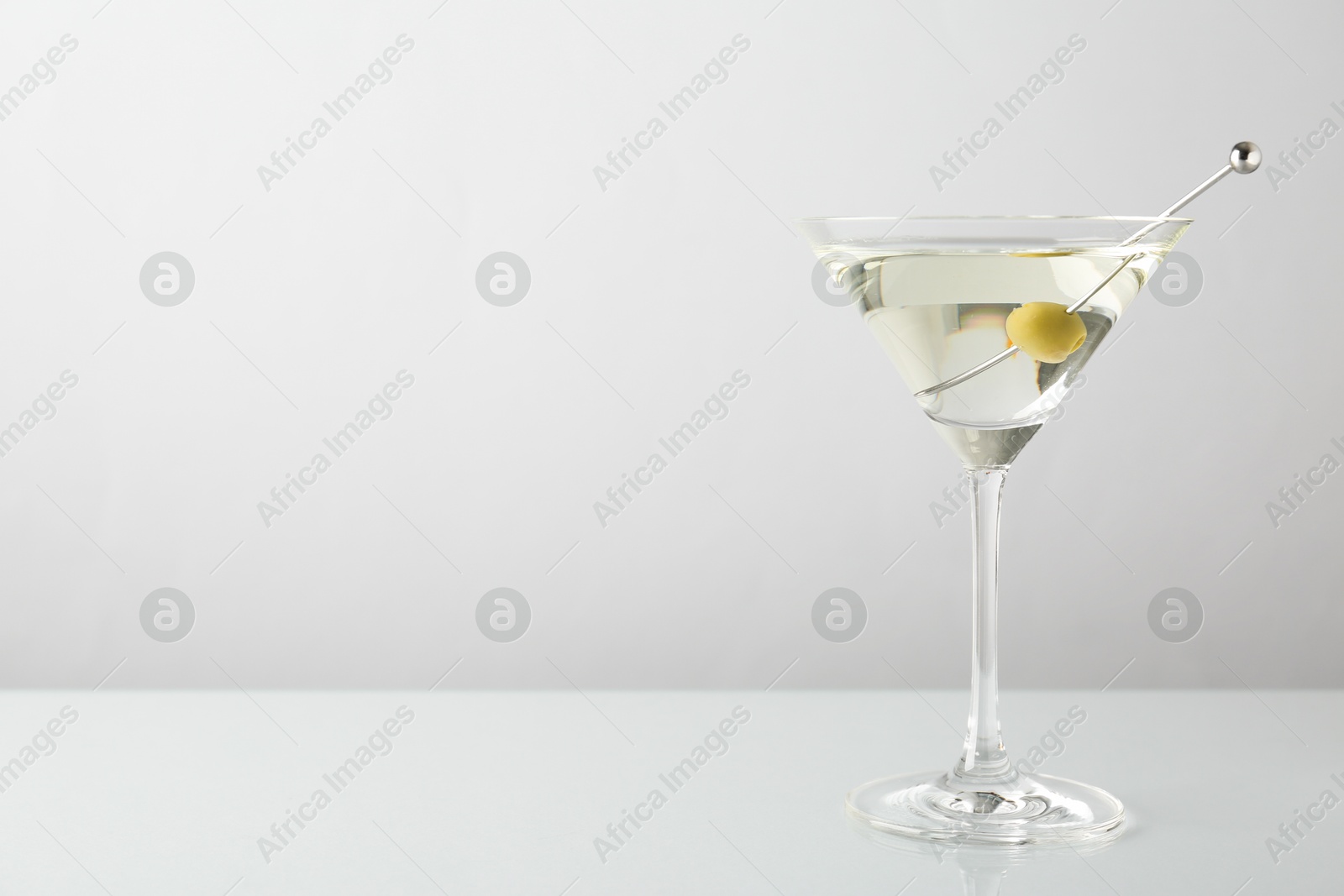 Photo of Martini cocktail with olive in glass on light table, space for text