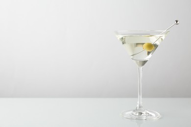 Photo of Martini cocktail with olive in glass on light table, space for text