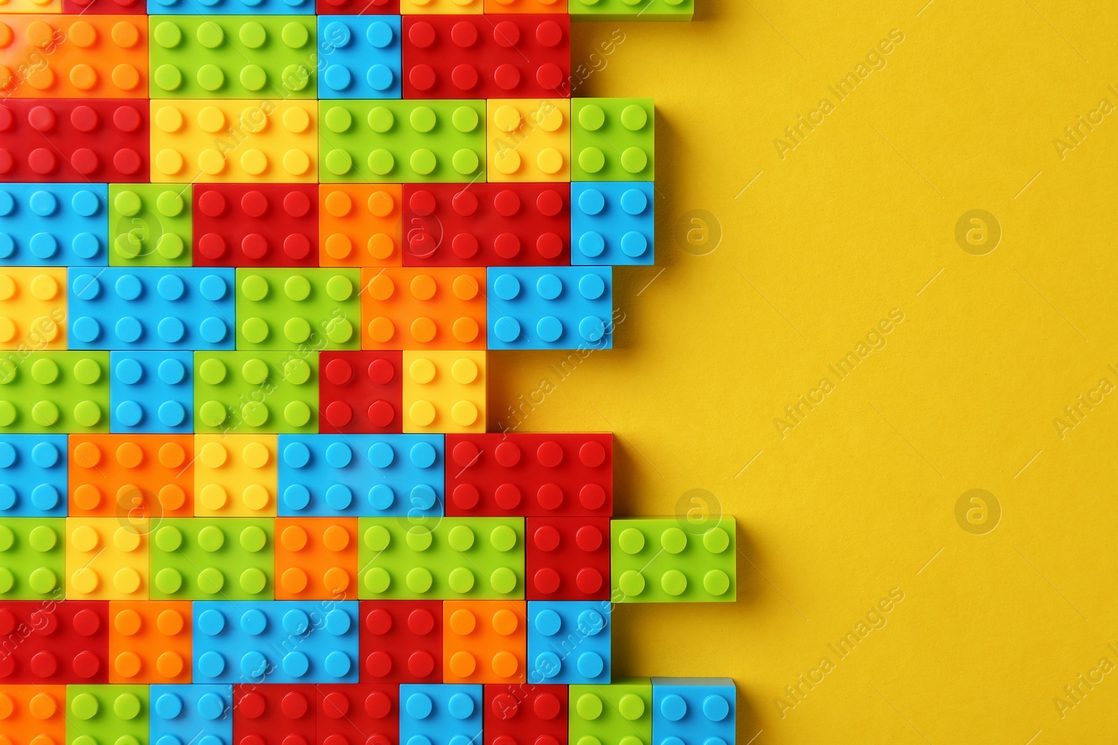 Photo of Constructor toy. Many colorful building blocks on yellow background, top view. Space for text