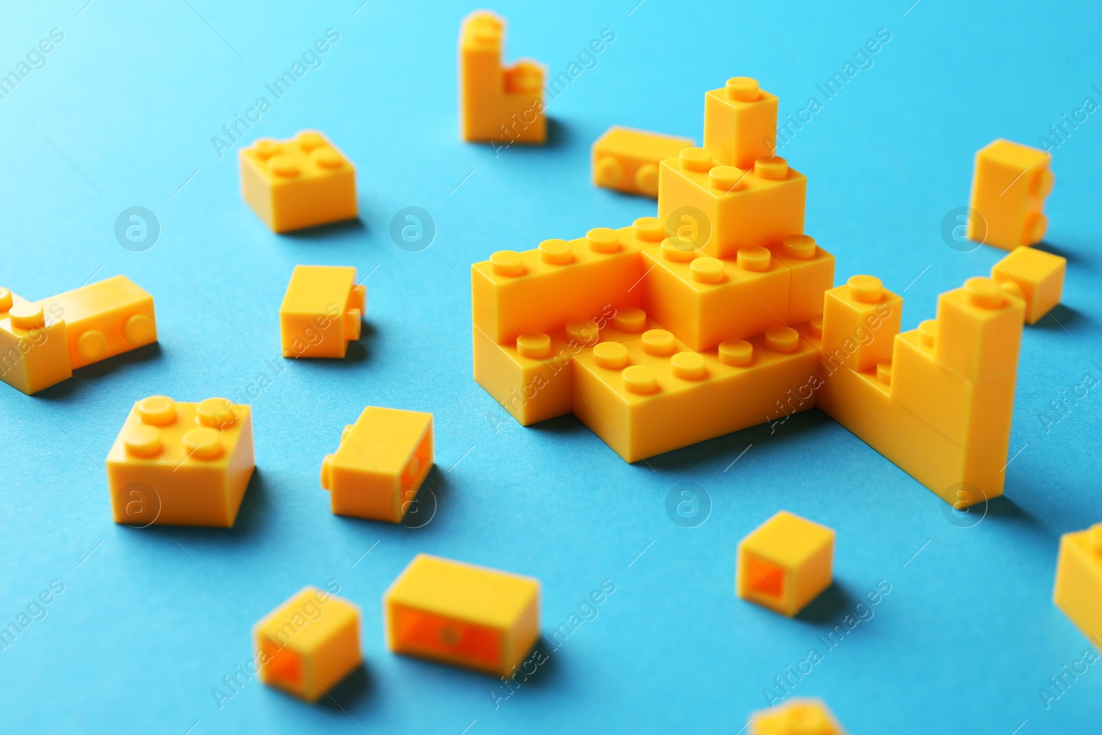 Photo of Constructor toy. Many yellow building blocks on light blue background, closeup