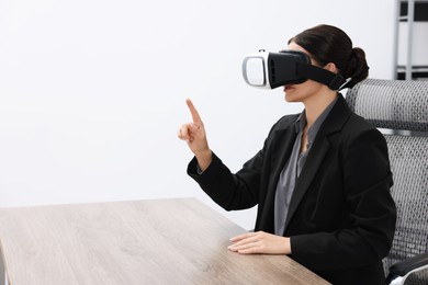 Photo of Woman using virtual reality headset in office, space for text