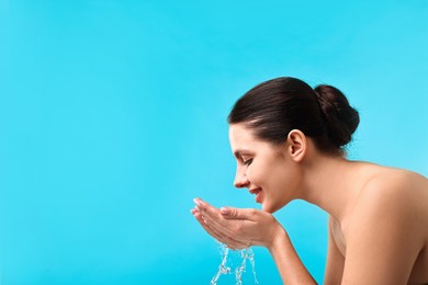 Photo of Smiling woman washing her face on light blue background. Space for text