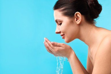 Photo of Attractive woman washing her face on light blue background. Space for text