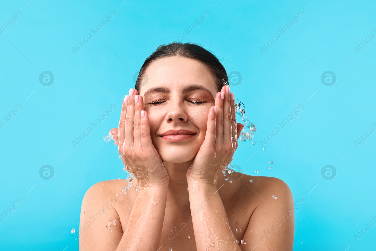 Photo of Attractive woman washing her face on light blue background