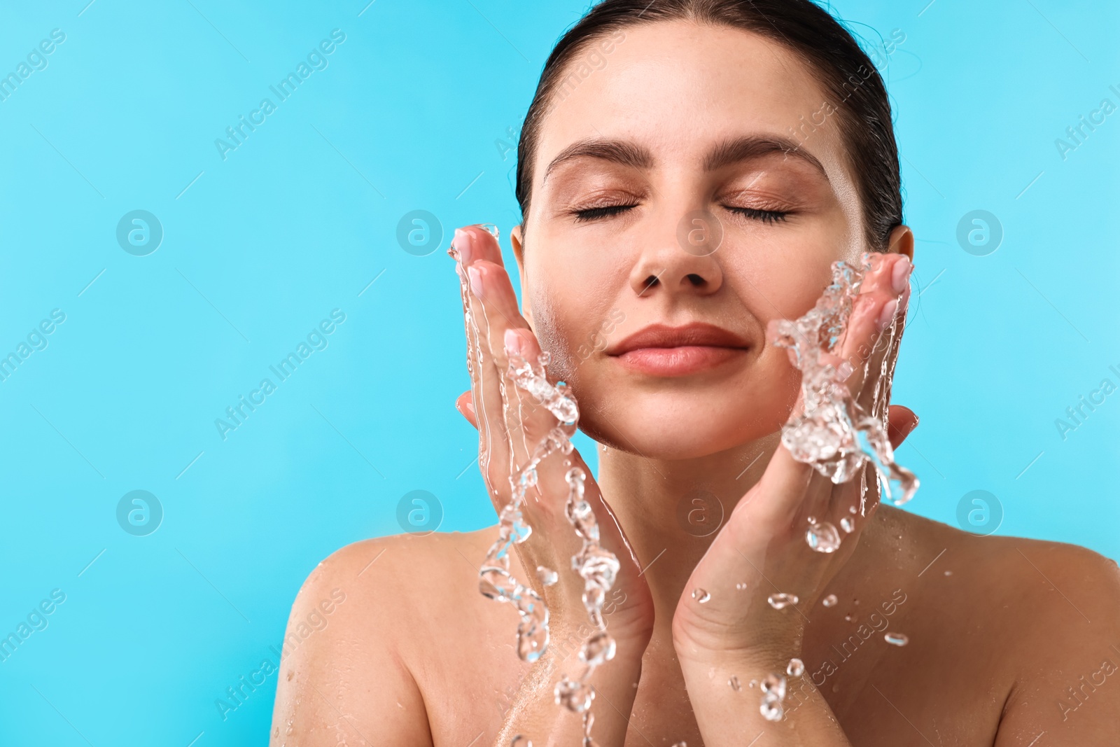 Photo of Attractive woman washing her face on light blue background. Space for text