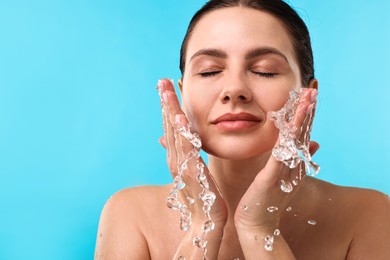 Photo of Attractive woman washing her face on light blue background. Space for text