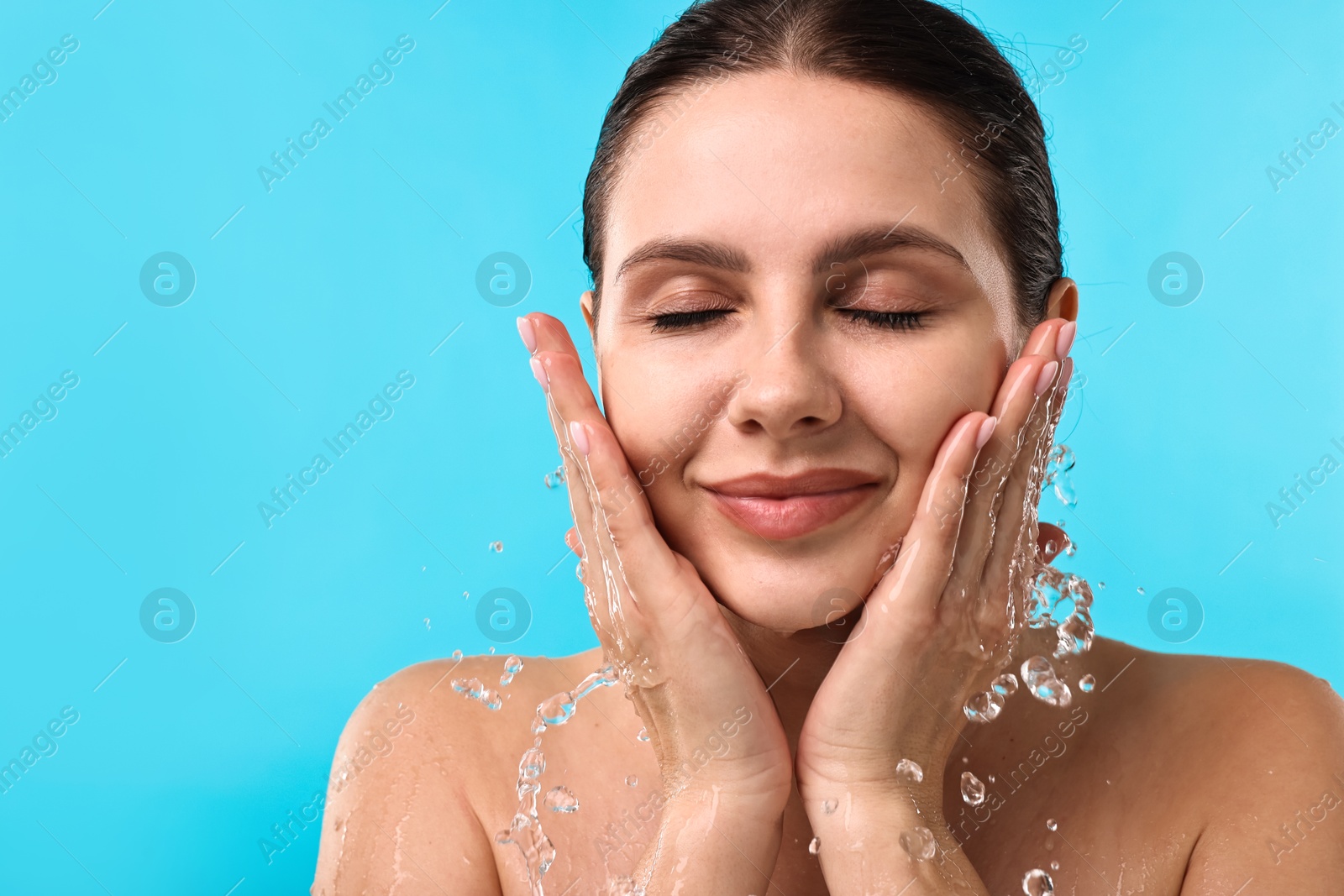 Photo of Attractive woman washing her face on light blue background. Space for text