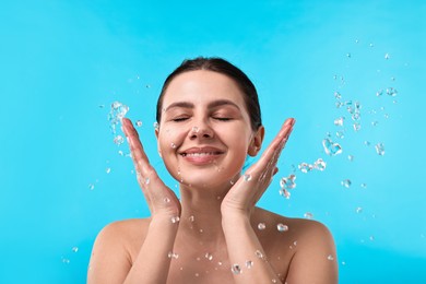 Smiling woman washing her face on light blue background