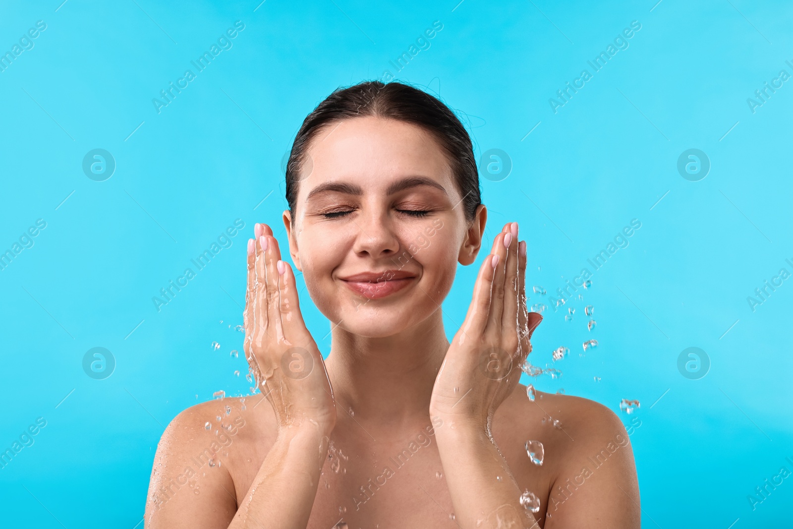 Photo of Attractive woman washing her face on light blue background