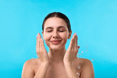 Photo of Attractive woman washing her face on light blue background