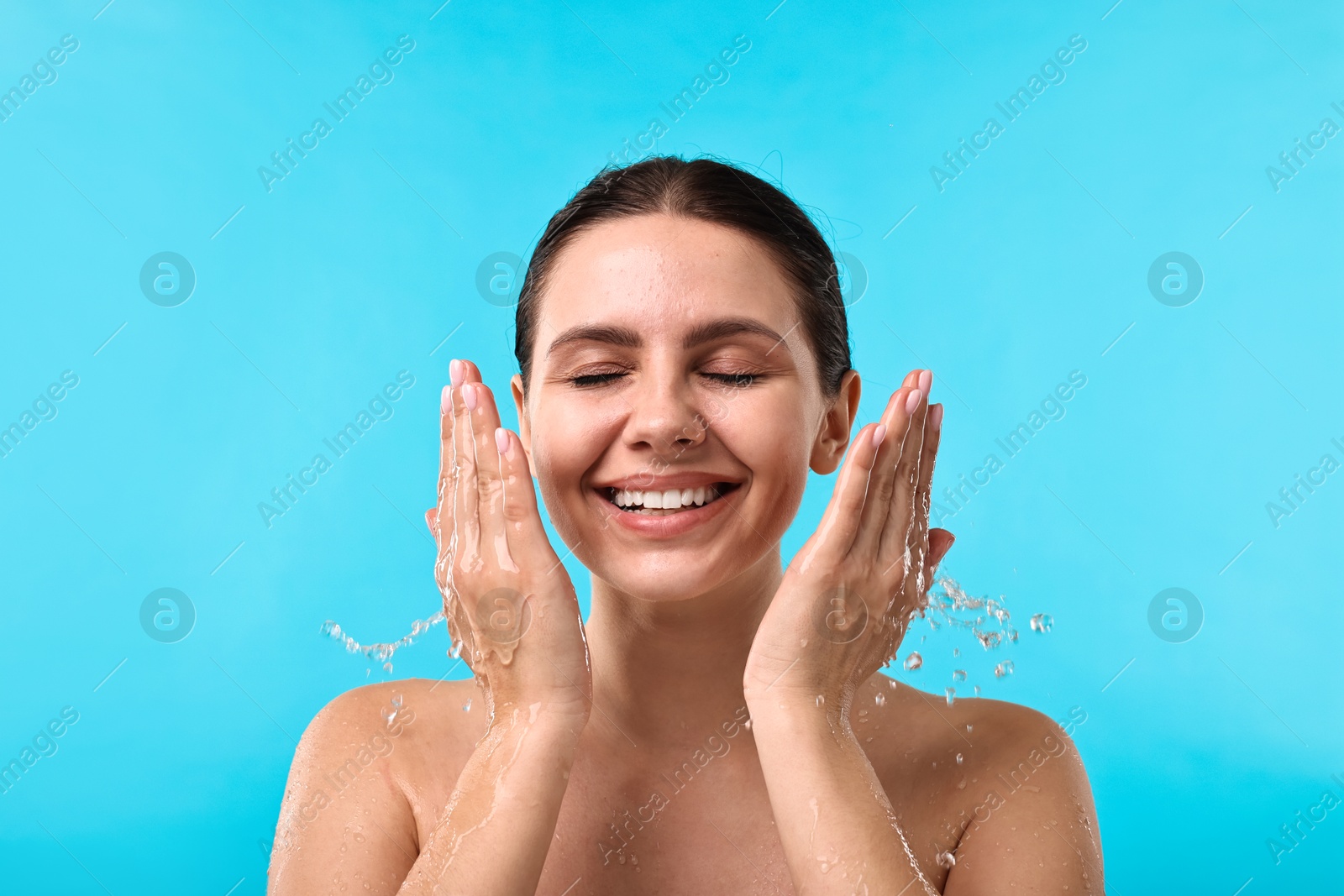 Photo of Smiling woman washing her face on light blue background