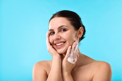 Photo of Smiling woman washing her face with cleansing foam against light blue background