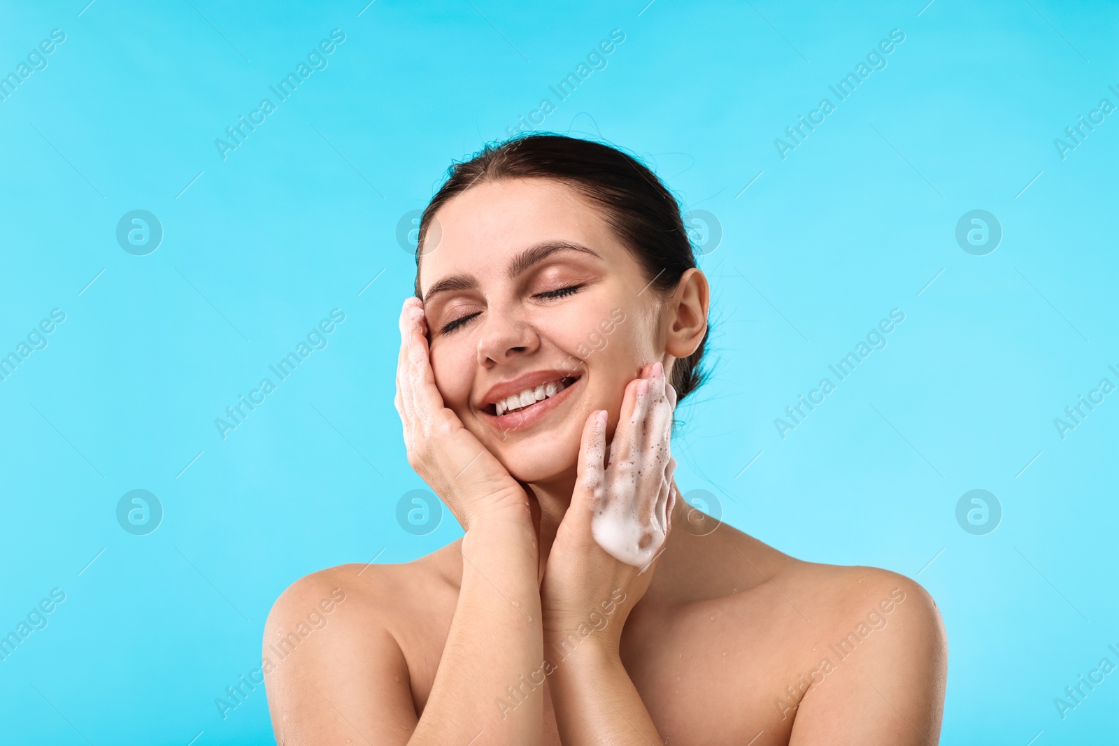 Photo of Smiling woman washing her face with cleansing foam against light blue background