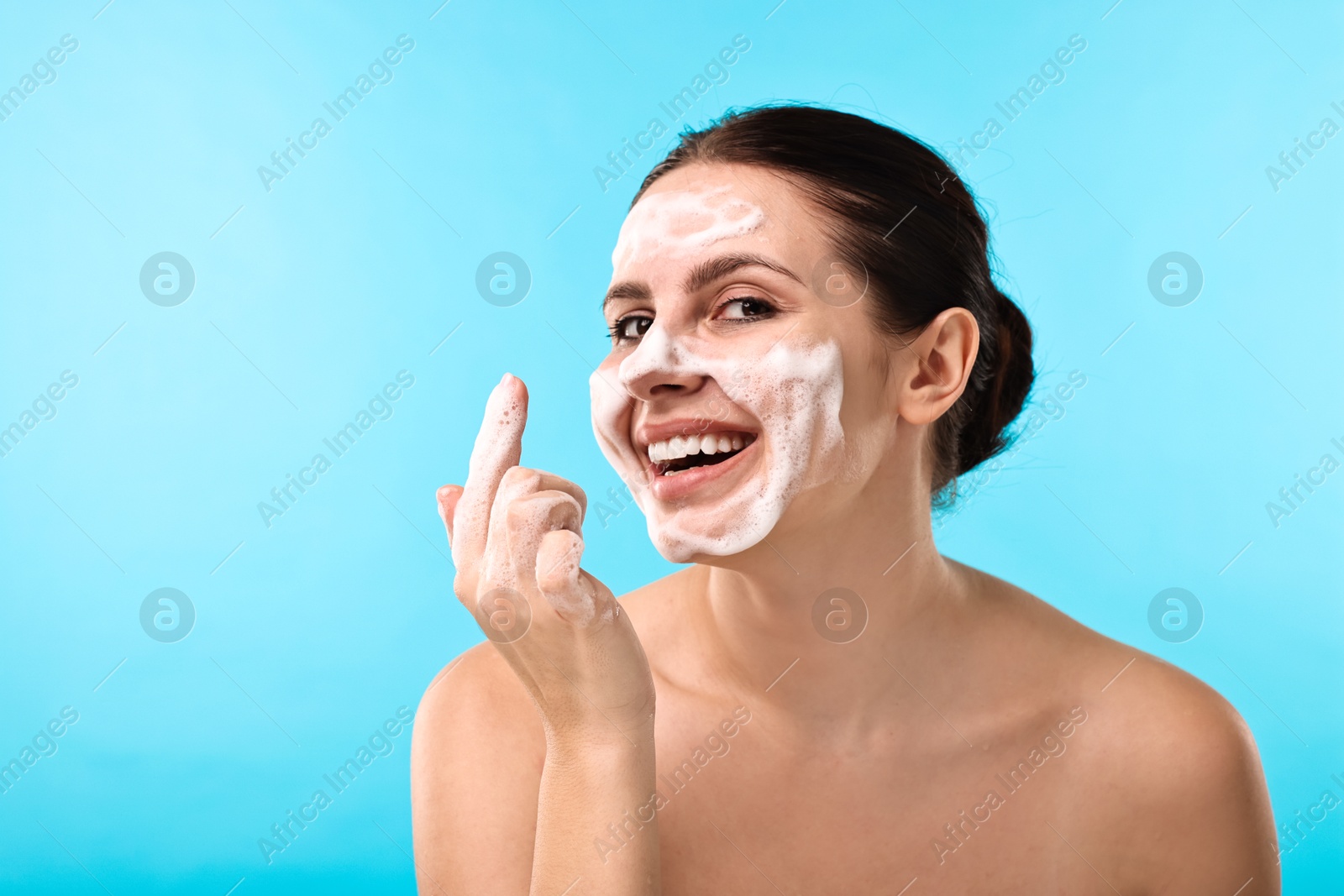 Photo of Smiling woman with cleansing foam on her face against light blue background, space for text. Washing routine