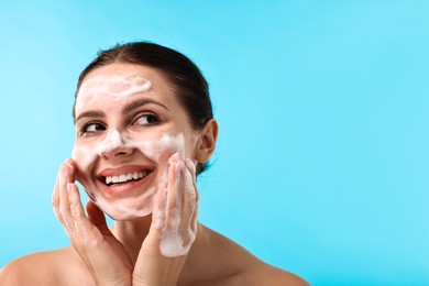 Photo of Smiling woman washing her face with cleansing foam on light blue background, space for text