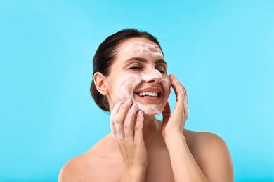 Photo of Smiling woman washing her face with cleansing foam on light blue background