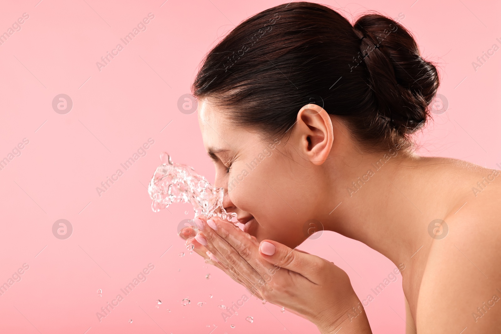 Photo of Attractive woman washing her face on pink background. Space for text