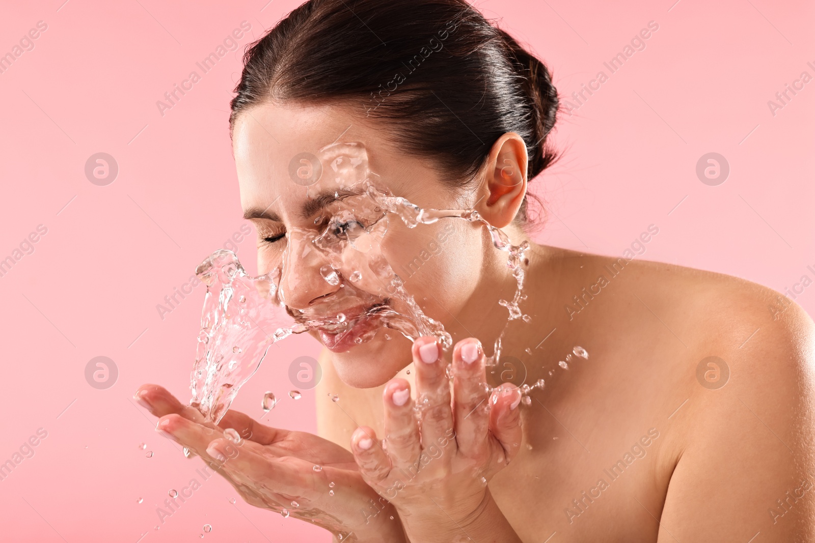 Photo of Attractive woman washing her face on pink background